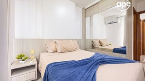 Un dormitorio moderno con una cama grande, una mesita de noche con lámpara, un espejo y un equipo de aire acondicionado.
