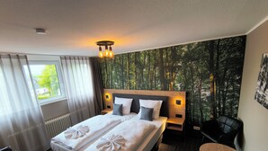 Quarto de hotel com uma cama grande, uma escrivaninha, uma cadeira e vista para uma floresta pela janela.