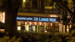 Exterior do Hotel Vakantie De Lange Man à noite, com letreiros iluminados e uma varanda.