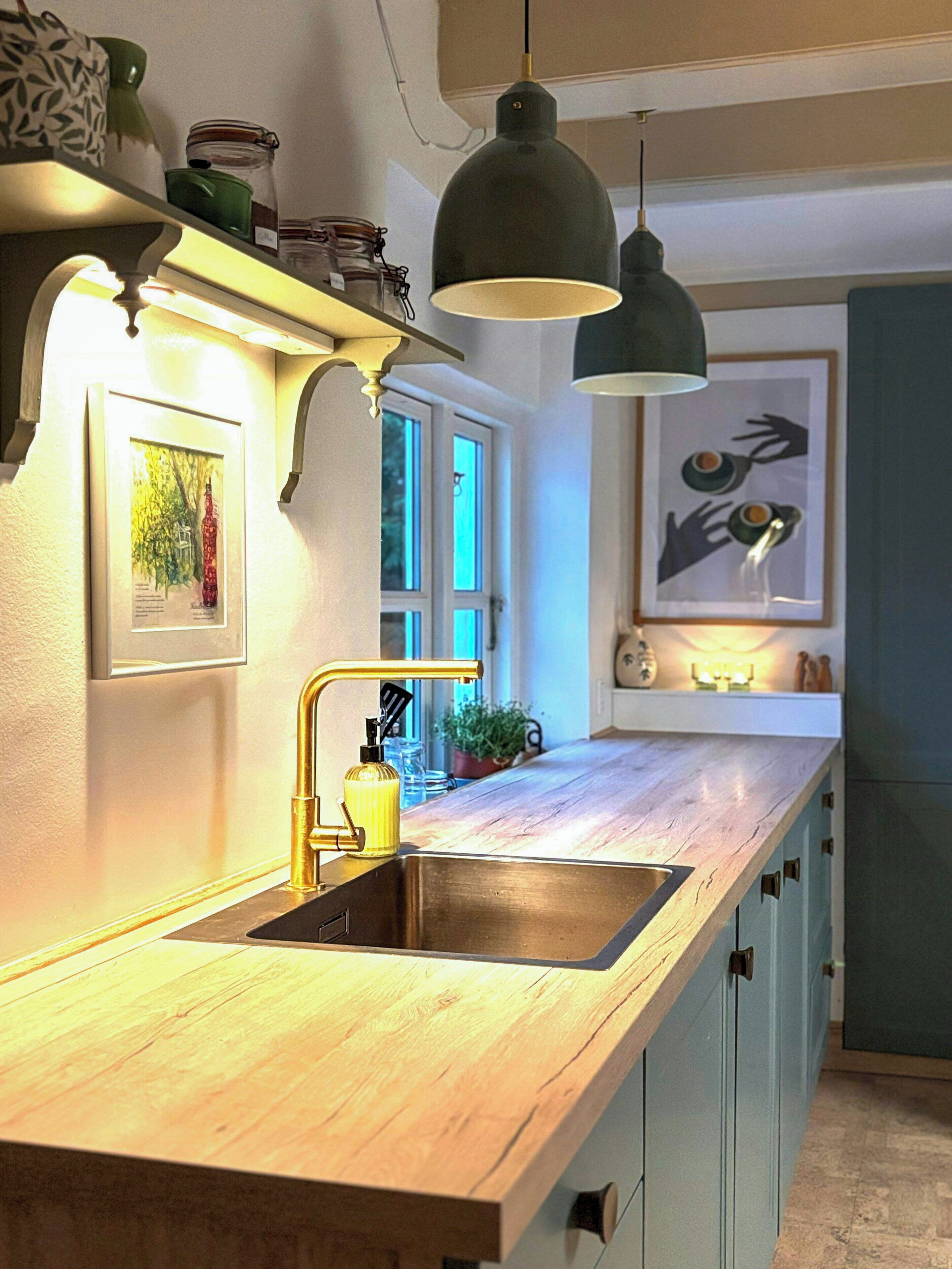 Une cuisine avec un plan de travail en bois, un évier, des luminaires suspendus et une fenêtre.