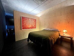 Ein Zimmer mit einem Bett, einem Nachttisch mit Lampe, einem großen abstrakten Gemälde an der Wand und einem Fernseher links.