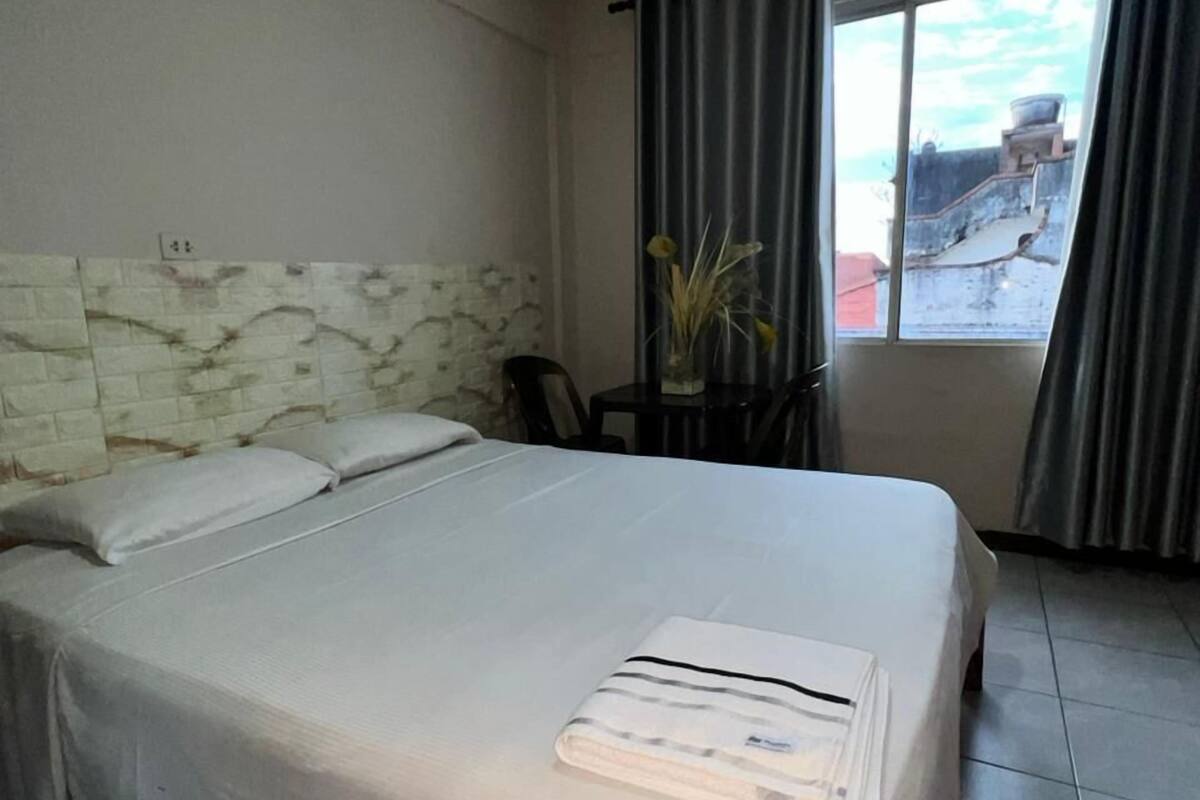 Habitación de hotel con cama, cabecero, ventana con cortinas y vistas al exterior.