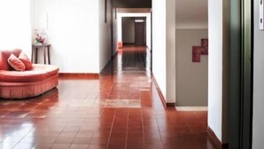 A hotel corridor with a red-tiled floor, a seating area with a red sofa, and a door on the right.