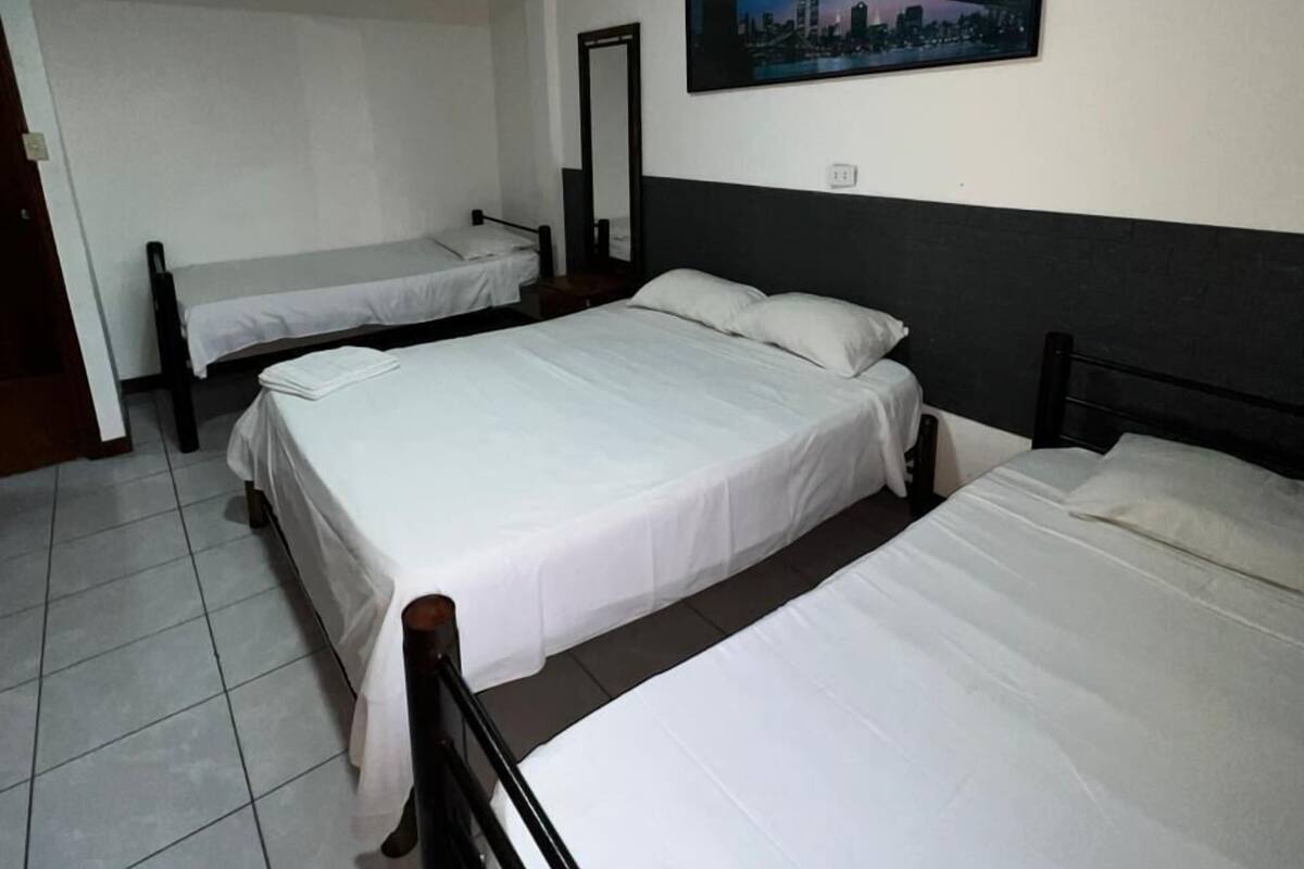 Habitación de hotel con dos camas, un espejo grande y una pintura de un paisaje urbano en la pared.