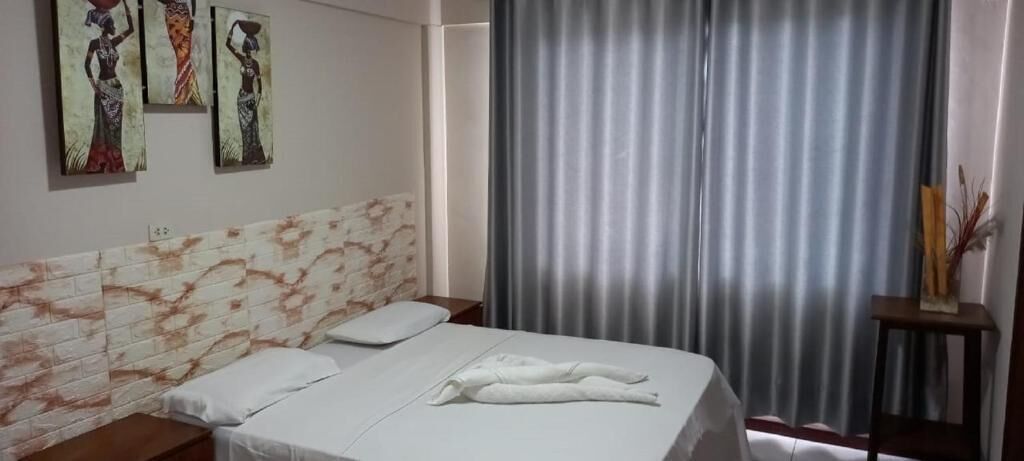 A hotel room with a bed, a headboard with a marble-like pattern, a window with curtains, and three wall-mounted artworks.