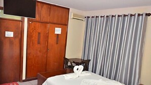 A hotel room with a bed, a wooden wardrobe, a desk, and a chair.