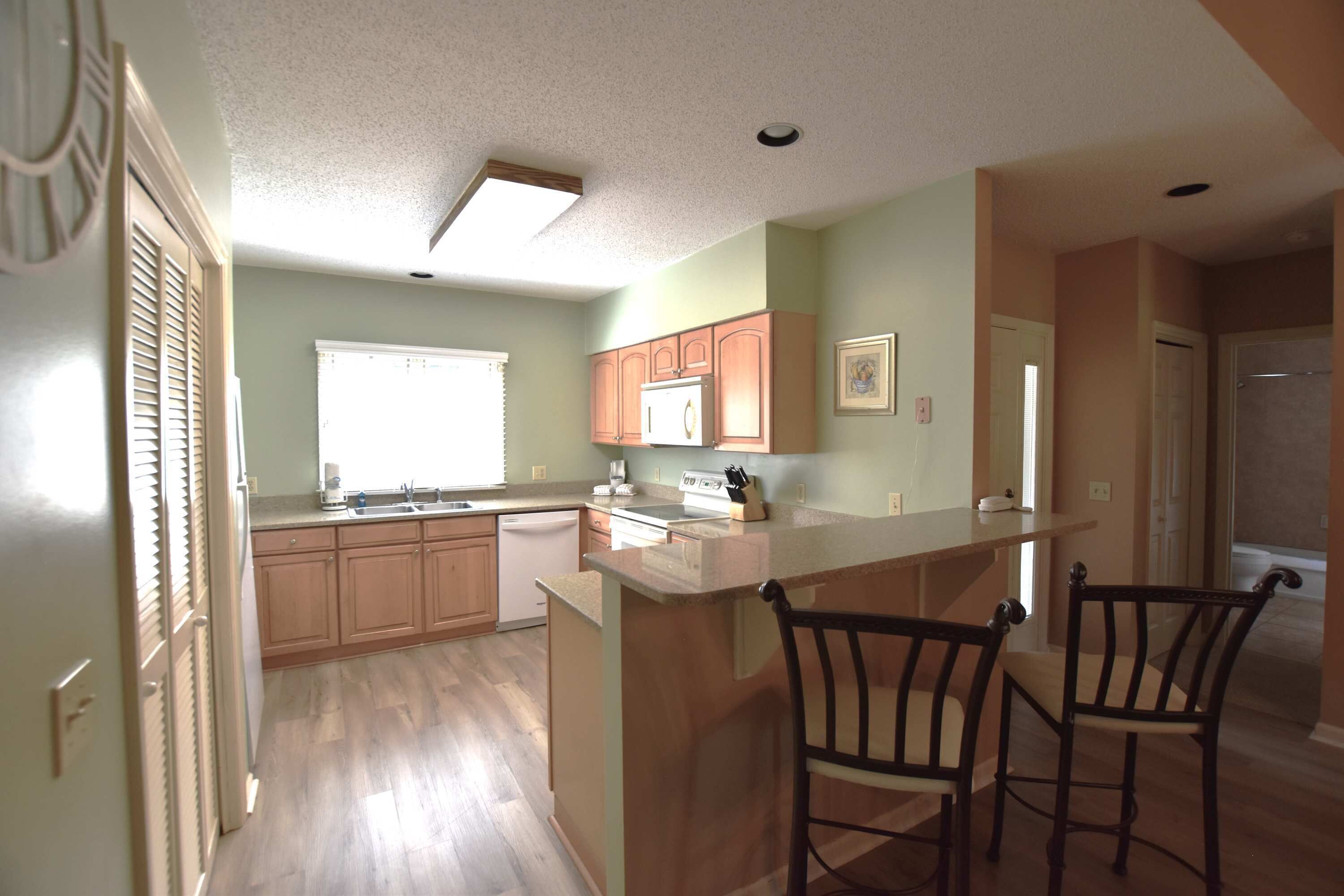 A kitchen with wooden cabinets, a microwave, and a bar area with two chairs.