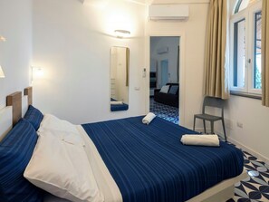 A hotel room with a bed, a chair, a mirror, and a window with curtains. - Seaside house with terrace in Atrani (Ravello)