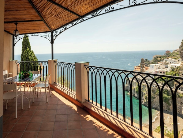 Eine Terrasse mit Tisch und Stühlen, mit Blick auf die Küste, Gebäude und Klippen.