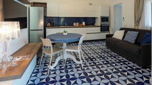 Eine moderne Küche mit weißen Schränken, einer blauen Fliesenrückwand und einem Essbereich mit rundem Tisch und Stühlen.