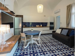 Eine moderne Küche mit weißen Schränken, einer blauen Fliesenrückwand und einem Essbereich mit rundem Tisch und Stühlen.