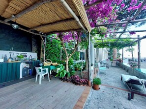 An outdoor patio with a bamboo roof, a table with chairs, potted plants, and a small cart. - Seaside house with terrace in Atrani (Ravello)