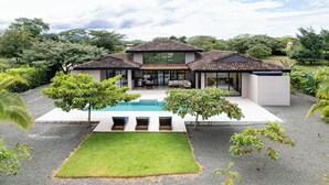 Une maison moderne avec une piscine, entourée d’un jardin bien entretenu et d’arbres.