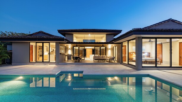 Une maison moderne dotée d’une piscine, de grandes fenêtres et d’un espace patio.