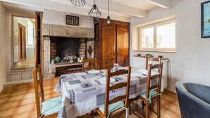 A dining area with a fireplace, wooden chairs, a table set for four, and hanging pendant lights. - Les Escapades - à 10min en voiture de la plage (Saint-Quay-Perros)