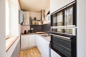 Ett kompakt kök med diskmaskin, ugn och ett fönster med gardiner.