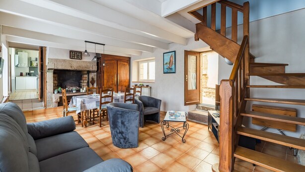A spacious living area with a fireplace, a wooden staircase, and a dining area with chairs and a table. - Les Escapades - à 10min en voiture de la plage (Saint-Quay-Perros)