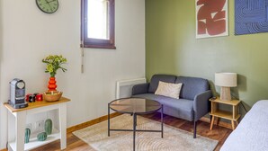 Une pièce comprenant un canapé, une table basse, une horloge, une fenêtre et un mur orné d’œuvres d’art abstraites.