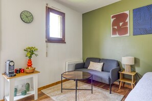 Ein Zimmer mit einer Couch, einem Couchtisch, einer Uhr, einem Fenster und einer Wand mit abstrakter Kunst.