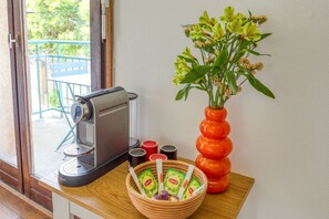 Eine Kaffeemaschine, eine Schale mit Lipton-Teebeuteln und ein Blumenvasen auf einem Holztisch.
