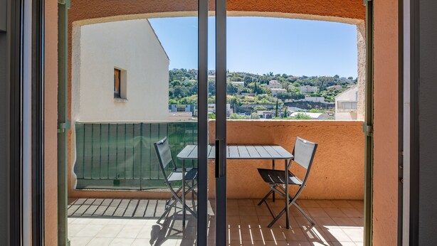 A balcony with a table and chairs, a view of a town, and a building with a green wall. - L’Escapade du Ponant - À 3 km de la plage (Saint Raphael)