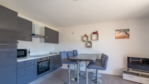 A modern kitchen with grey cabinets, a microwave, and a dining area with a table and chairs. - L’Escapade du Ponant - À 3 km de la plage (Saint Raphael)