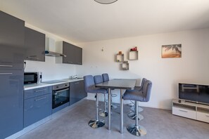 A modern kitchen with grey cabinets, a microwave, and a dining area with a table and chairs. - L’Escapade du Ponant - À 3 km de la plage (Saint Raphael)