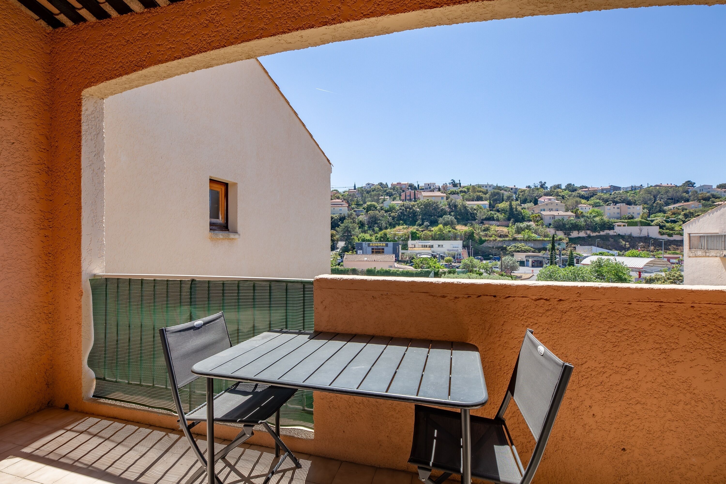 A balcony with a table and chairs, a view of a hillside town, and a small window.