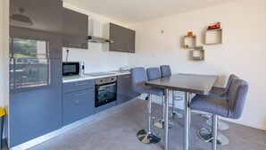 A modern kitchen with grey cabinets, a microwave, oven, and a dining area with a table and chairs. - L’Escapade du Ponant - À 3 km de la plage (Saint Raphael)
