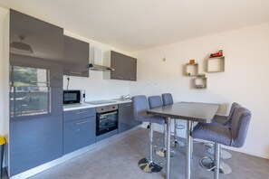 A modern kitchen with grey cabinets, a microwave, oven, and a dining area with a table and chairs. - L’Escapade du Ponant - À 3 km de la plage (Saint Raphael)