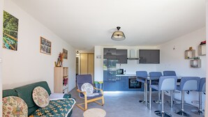 A modern living room with a sofa, a round coffee table, a dining area with bar stools, a kitchen with a microwave, and a ceiling light fixture. - L’Escapade du Ponant - À 3 km de la plage (Saint Raphael)