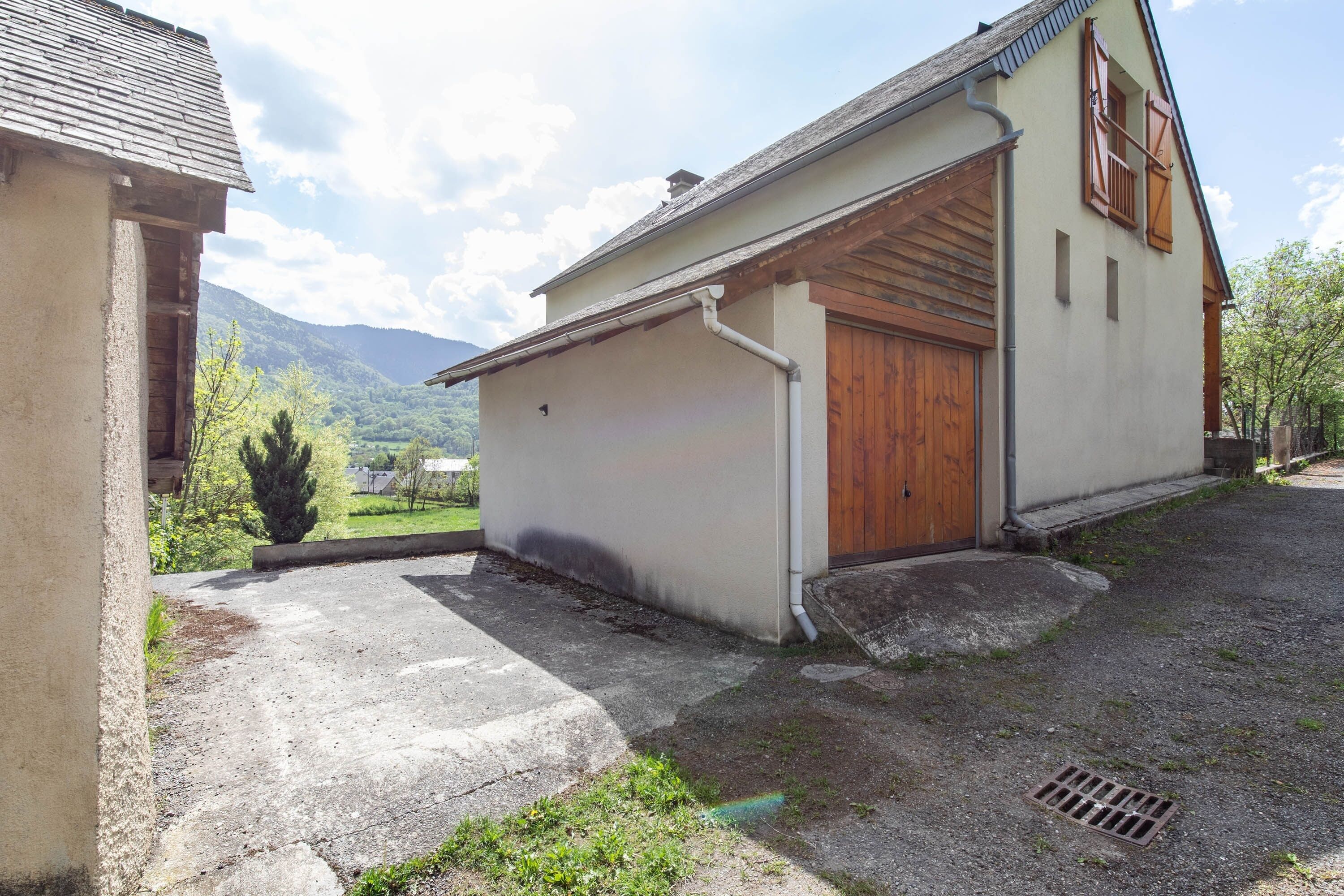 Un petit bâtiment avec un garage, une porte en bois et une allée en béton.