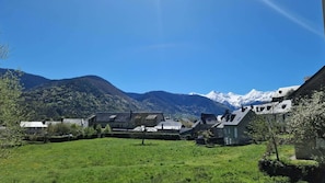 Ein ländliches Dorf mit traditionellen Häusern, einem grünen Feld und schneebedeckten Bergen im Hintergrund.