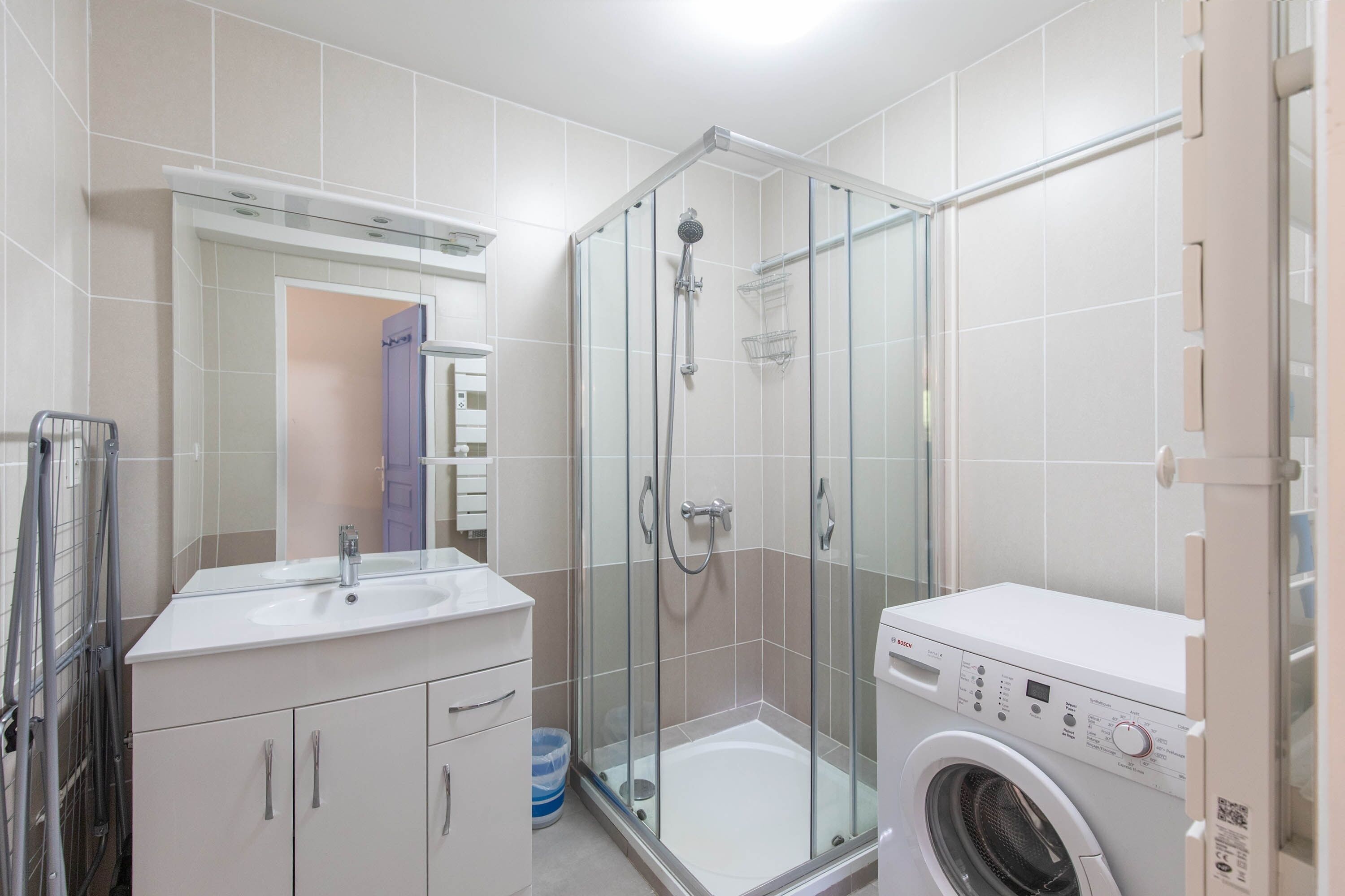 Een moderne badkamer met een douche met glazen wand, een wastafel en een voorlader wasmachine.