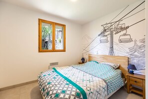 Ein Schlafzimmer mit Bett, Nachttisch, Lampe, Fenster und Wandgemälde.
