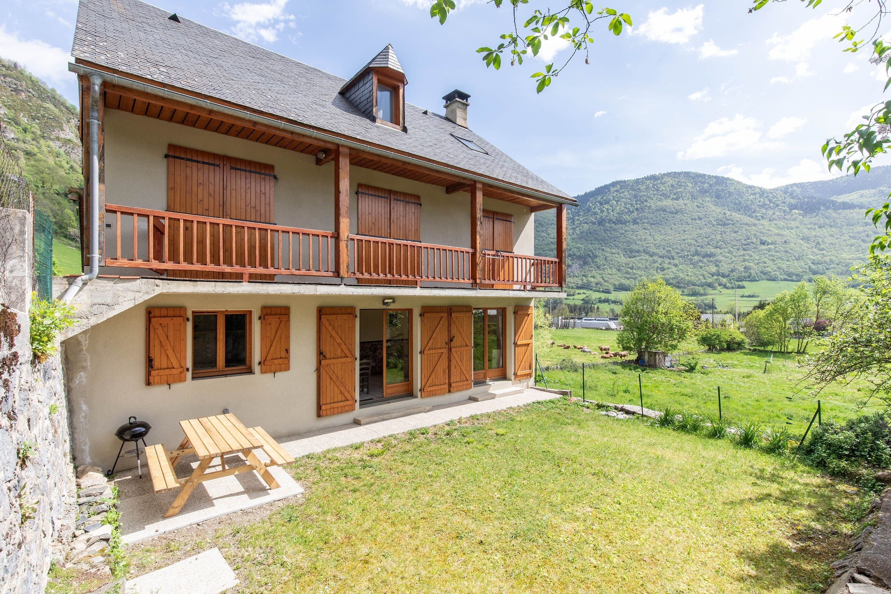 Une maison à deux étages avec un balcon, une table en bois et une vue sur une vallée verdoyante.