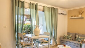 Une pièce comprenant une table à manger, des chaises, un canapé, une petite table ronde et une fenêtre avec des rideaux.