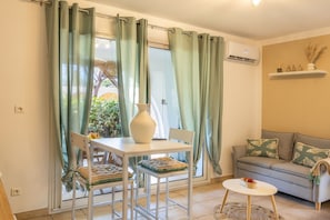 Ein Zimmer mit Esstisch, Stühlen, einer Couch, einem kleinen runden Tisch und einem Fenster mit Vorhängen.