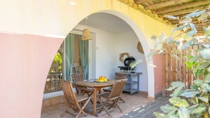 Un espace extérieur aménagé pour les repas, avec une table ronde, quatre chaises et un panier de fruits.