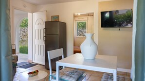 Une pièce comprenant une table blanche, une chaise blanche, un vase blanc, un téléviseur et un réfrigérateur.