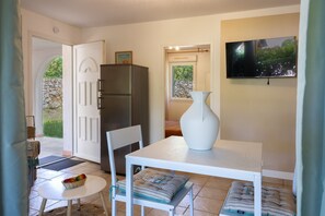 Ein Zimmer mit einem weißen Tisch, einem weißen Stuhl, einer weißen Vase, einem Fernseher und einem Kühlschrank.
