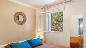 Une chambre à coucher avec un lit, une fenêtre donnant sur un mur de pierre, un miroir sur le mur et une table de chevet avec une lampe.