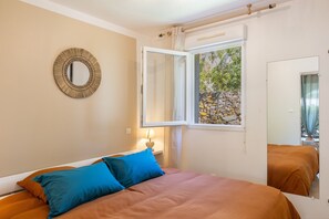 Ein Schlafzimmer mit Bett, einem Fenster mit Blick auf eine Steinmauer, einem Spiegel an der Wand und einem Nachttisch mit Lampe.