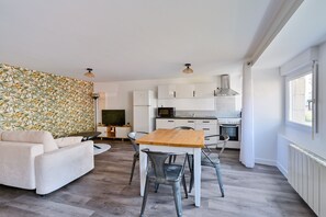 Une cuisine moderne avec des meubles blancs, une table à manger en bois et un canapé dans un coin salon agrémenté d’un mur à motifs.