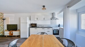 A modern kitchen with white cabinets, a microwave, stove, and a dining area with a wooden table and chairs. - L’Escale morbihannaise – Appt à 15 min de la plage (Muzillac)