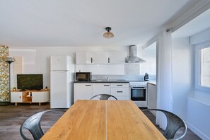 Une cuisine moderne avec des meubles blancs, un four à micro-ondes, une cuisinière et un coin repas comprenant une table et des chaises en bois.