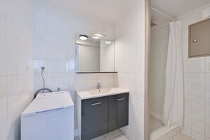 A bathroom with a white sink, dark cabinets, a mirror, and a shower area. - L’Escale morbihannaise – Appt à 15 min de la plage (Muzillac)