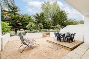 Un patio al aire libre con mesa y sillas, rodeado de arena y follaje.