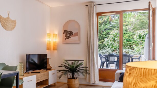 Ein modernes Wohnzimmer mit Flachbildfernseher, einer Zimmerpflanze, einer Couch und einem Essbereich mit Stühlen.