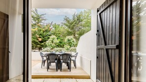 Eine offene Tür, die auf eine grüne Terrasse mit Tisch und Stühlen führt.